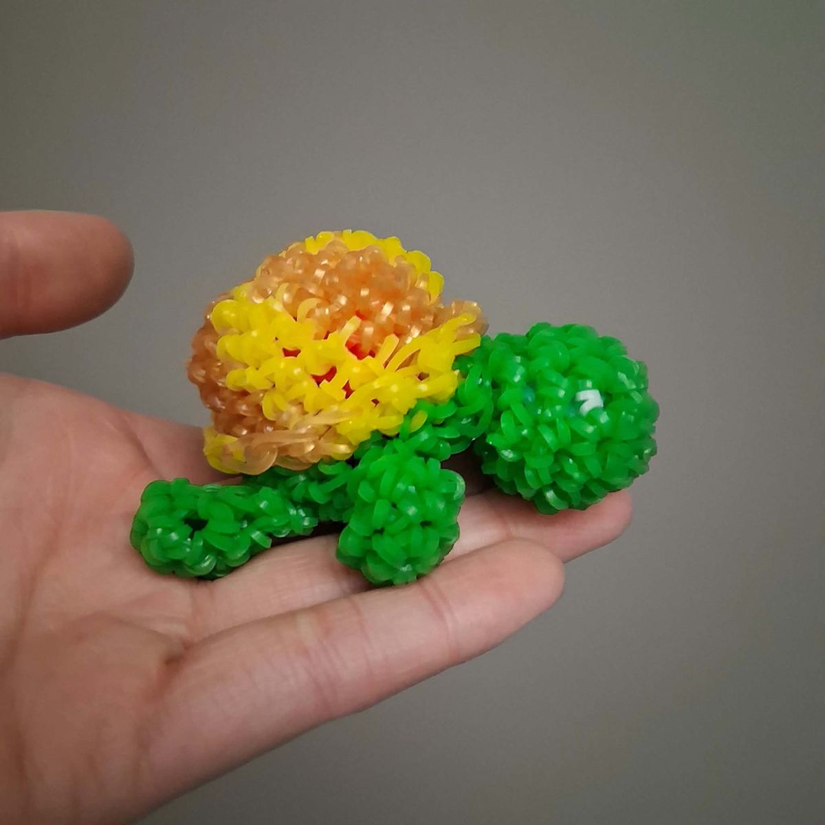 A small turtle made from yellow, orange, and green loom bands resting in someone's palm